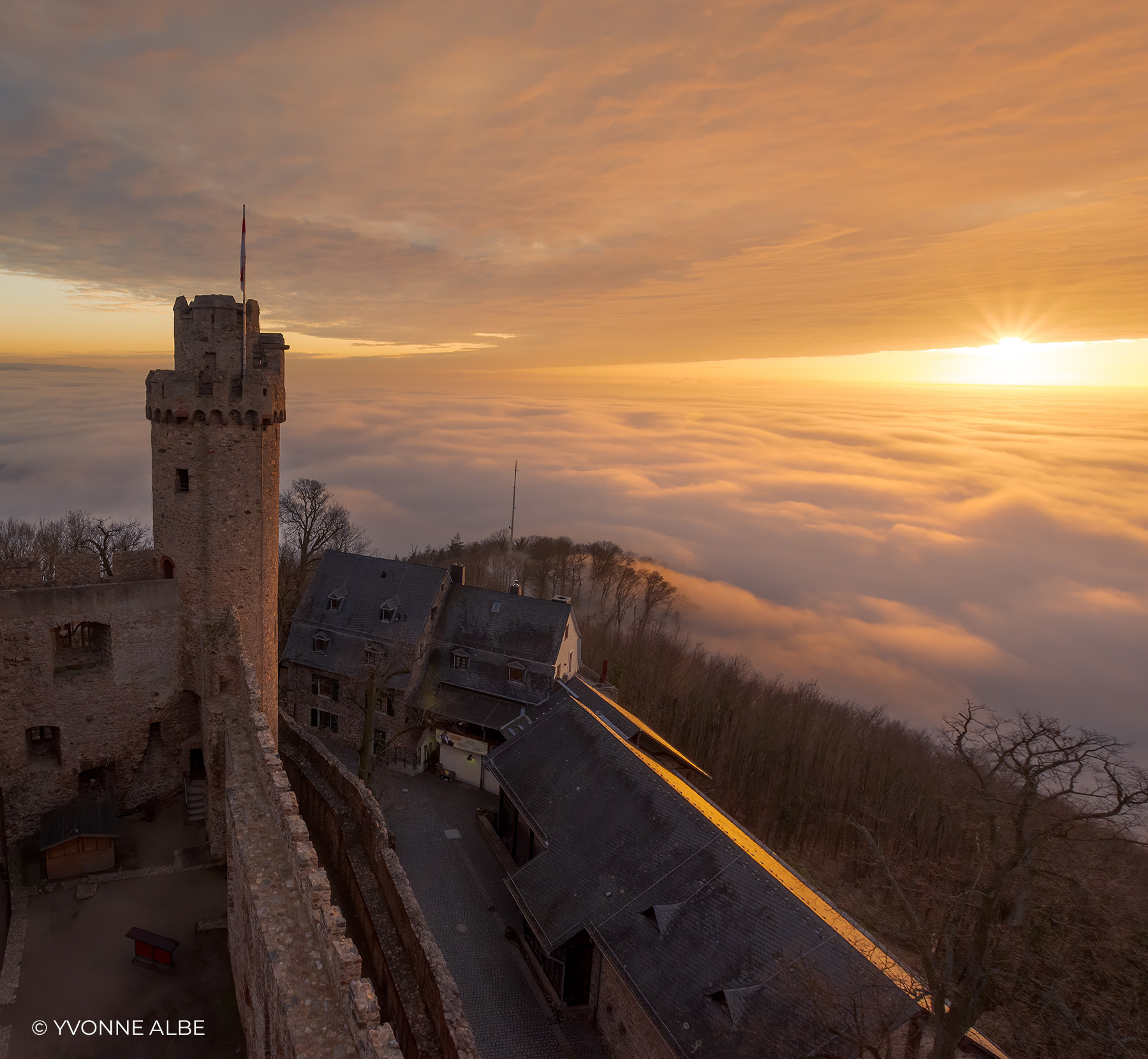Burganlage mit Turm über einem Nebelmeer bei Sonnenaufgang mit goldenem Himmel, Landschaftsfoto von Yvonne Albe