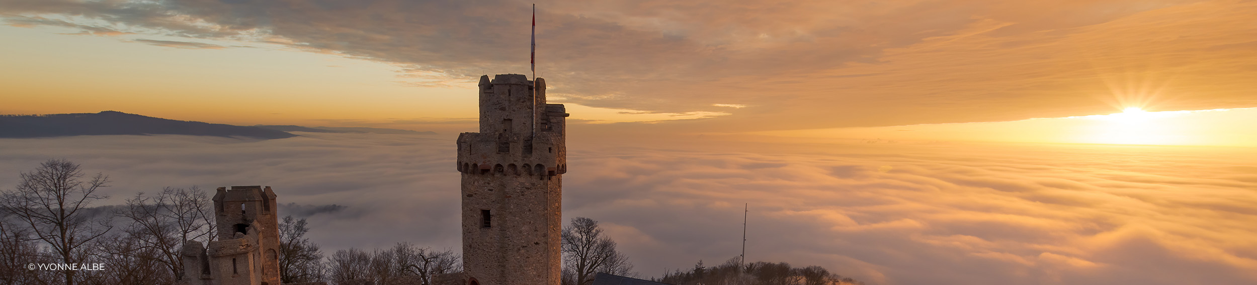 Kasteeltoren boven een zee van mist bij zonsopgang onder een gouden hemel, landschapsfoto van Yvonne Albe
